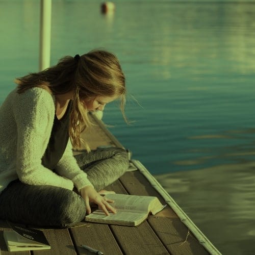 Lady by the water reading the bible